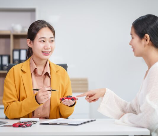 Asian businesswoman and a salesman discuss car sales, insurance, financing a customer at a desk